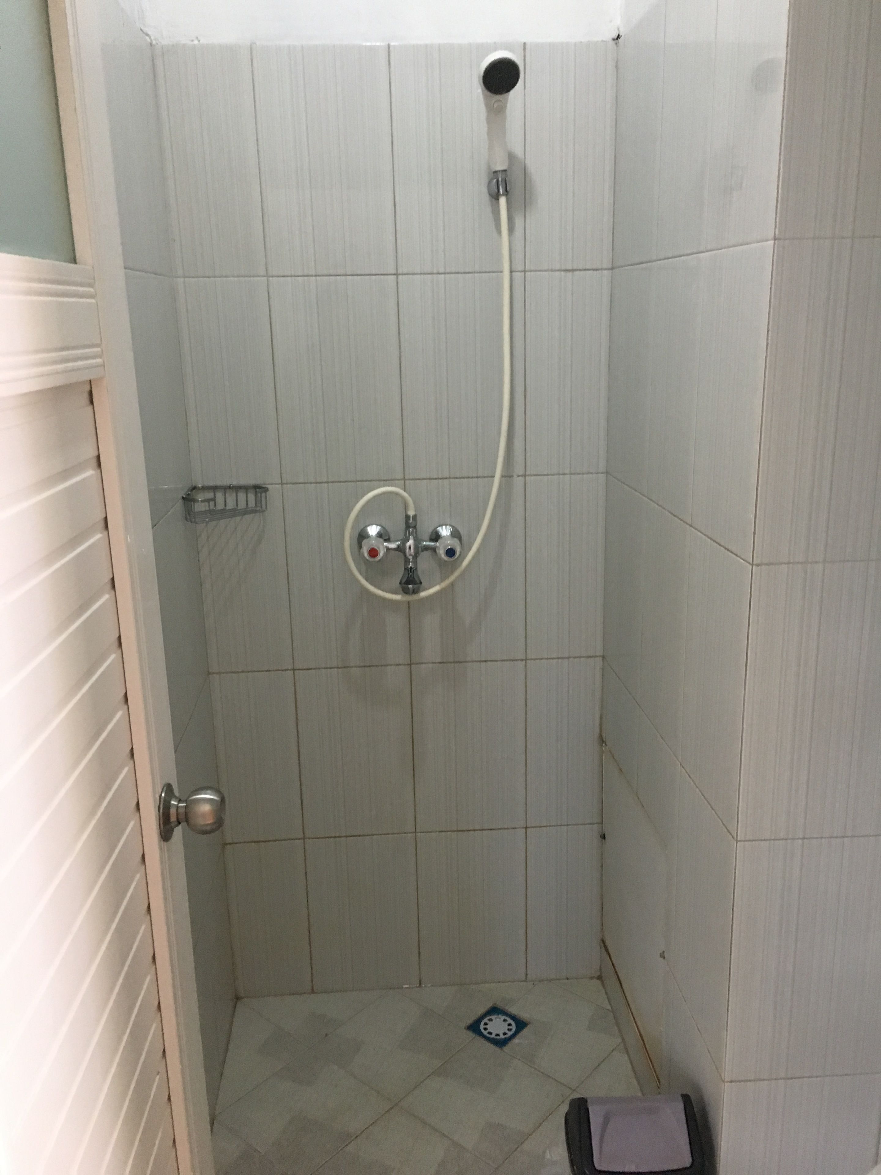 Un baño pequeño revestido de azulejos, con un cabezal de ducha de mano y un grifo empotrado en la pared.
