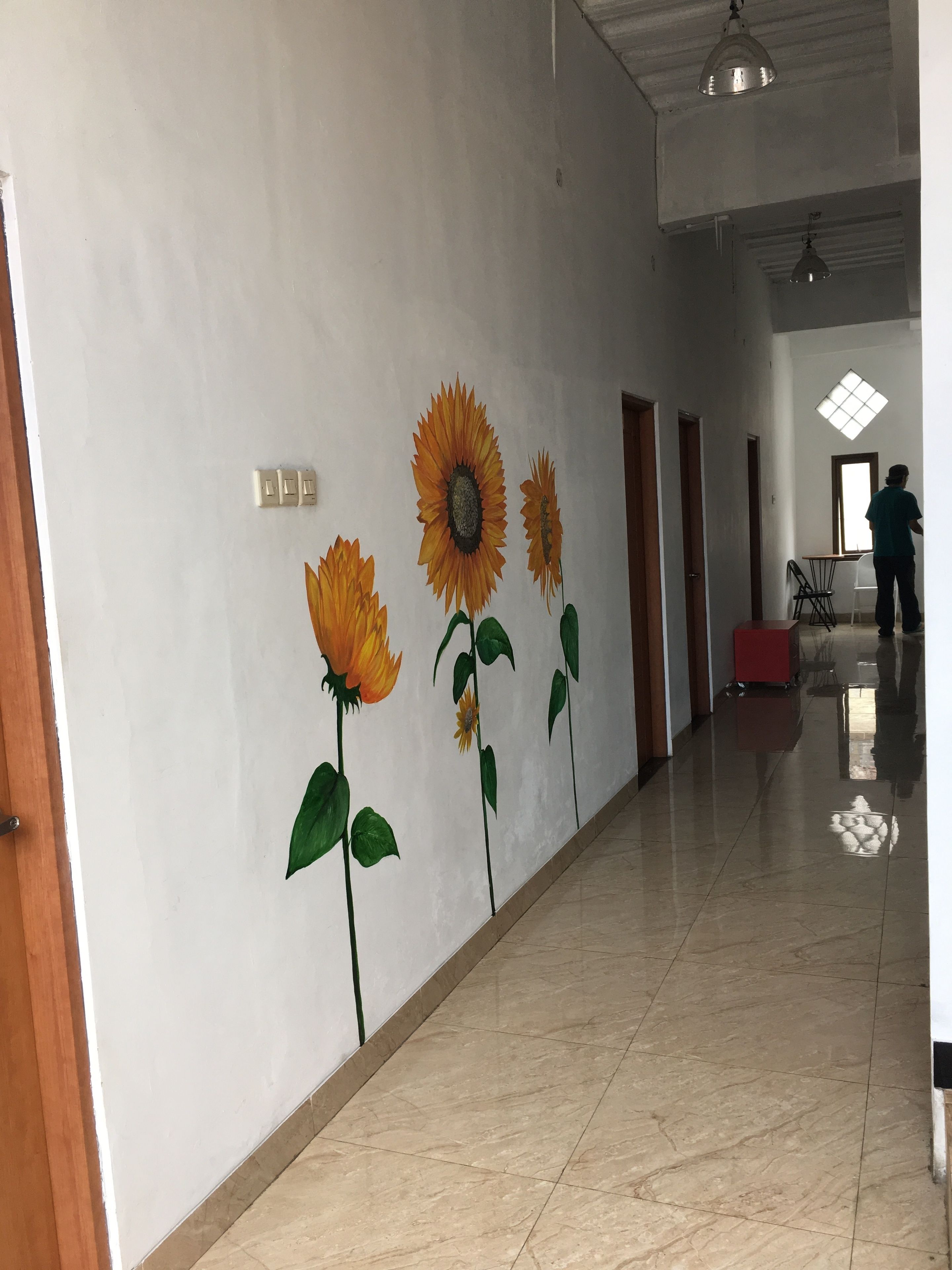 A hallway with a mural of sunflowers on the wall, a tiled floor, and a ceiling fan.