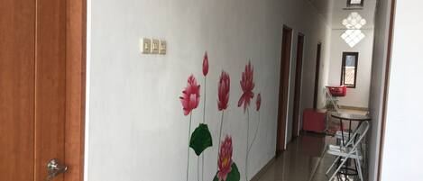 Een hal met een witte muur waarop een muurschildering van een lotusbloem is aangebracht. Links is een houten deur en in de rechterhoek staat een klein tafeltje met stoelen.