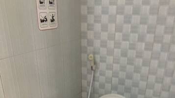 Uma casa de banho pequena, com azulejos, um autoclismo branco, um secador de mãos e um botão de descarga fixado na parede.