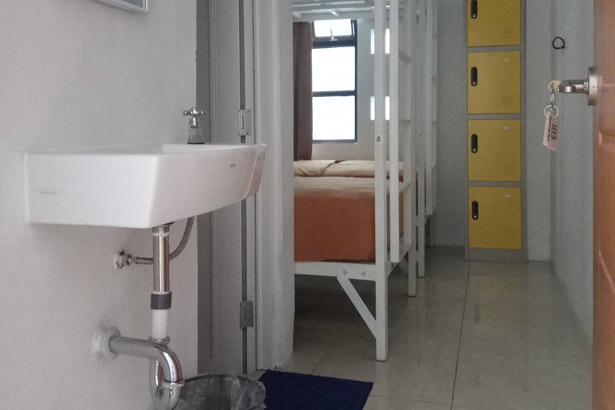 A dormitory room with bunk beds, a sink, and a trash bin.