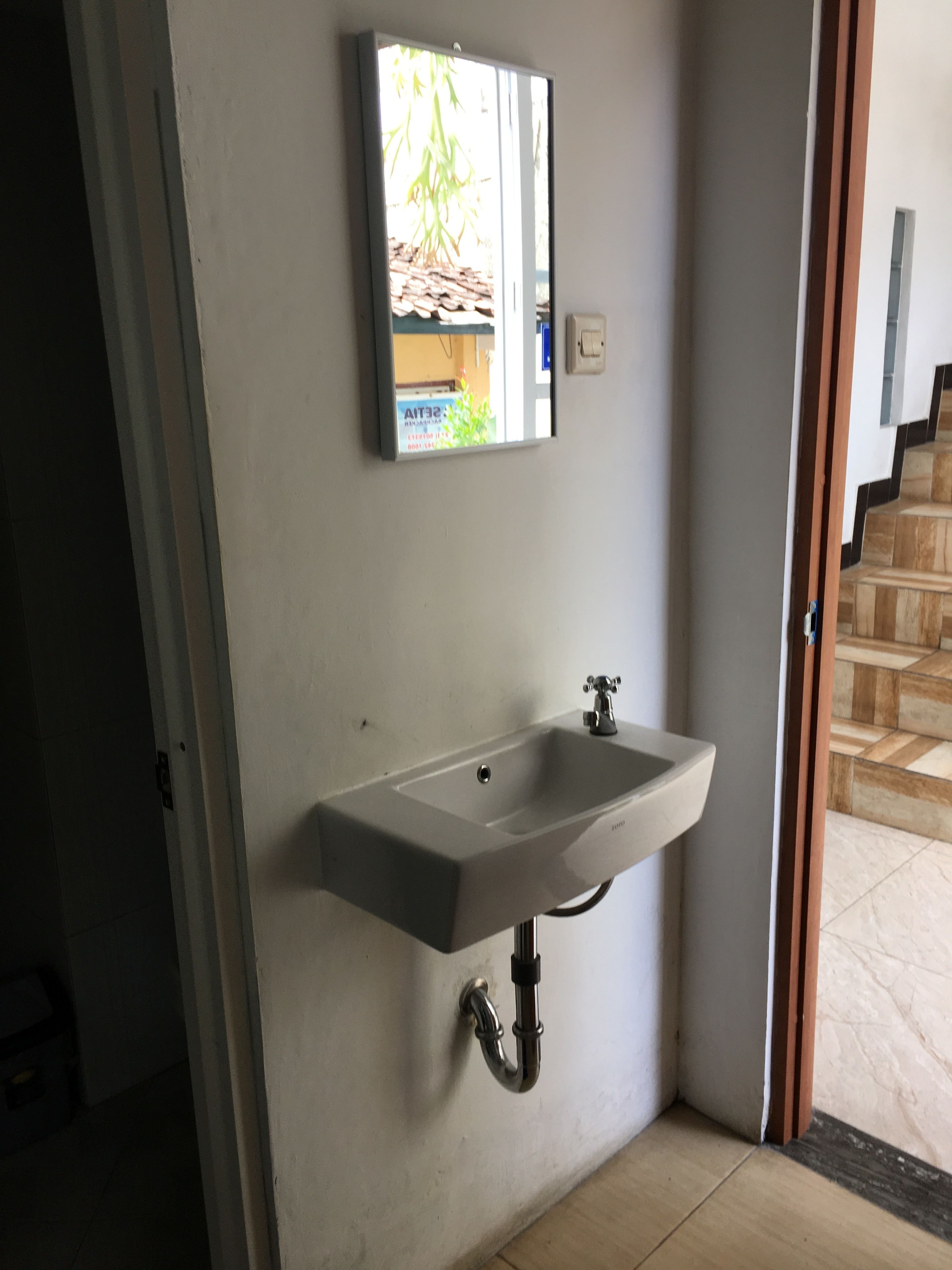 Un baño con un lavabo blanco, un espejo y vistas a una escalera.