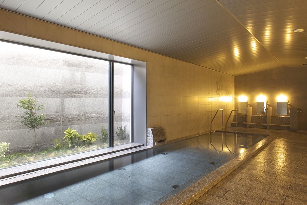 Piscina interior moderna com paredes de vidro transparente, chão em mosaico e vista para o exterior arborizado.