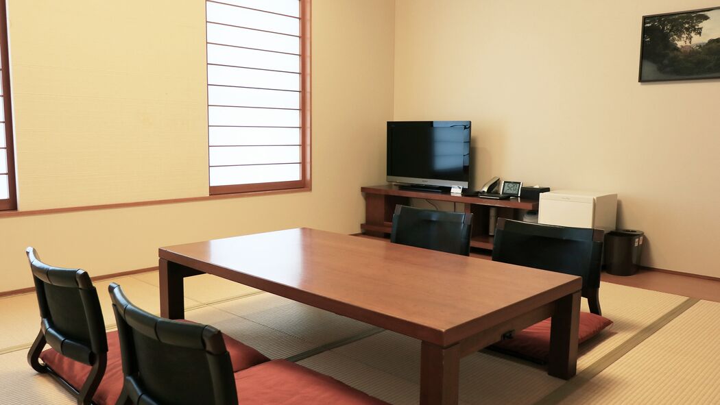 A room with a wooden table, four chairs, a television, and a window with blinds.