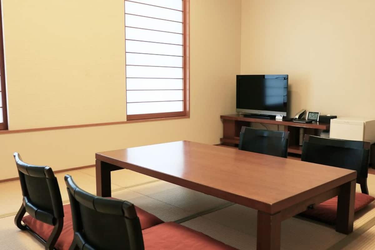 A room with a wooden table, four chairs, a television, and a window with blinds.