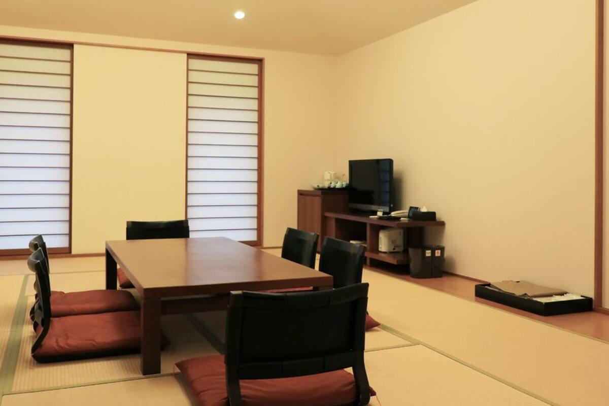 A traditional Japanese-style room with tatami flooring, a low table, and black chairs.