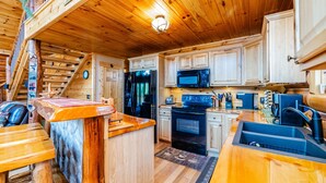 Interior de una cabaña de madera con cocina, una mesa de comedor y una escalera.