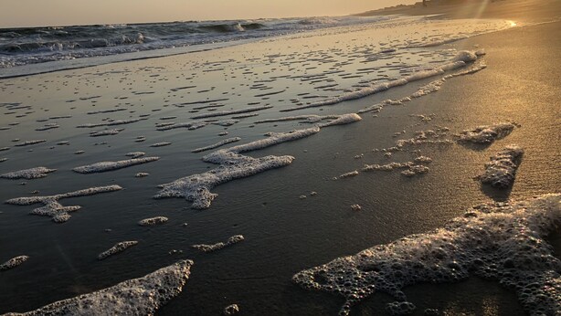 A beach with waves and footprints in the sand.