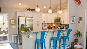 A modern kitchen with white cabinets, a central island with blue bar stools, stainless steel appliances, and pendant lighting.