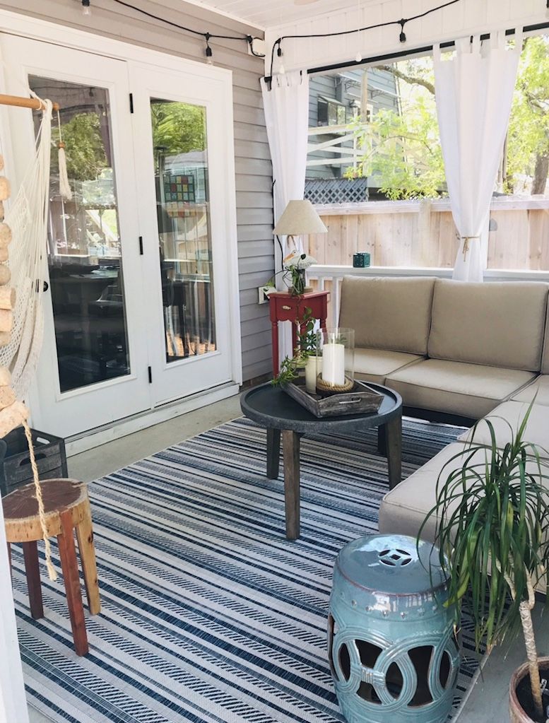 A cozy patio area with a sofa, a small table, a hanging chair, and a potted plant.