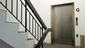 A staircase with black railings leading to an elevator marked with the letter 'G'. - Rica Hotel (Subang Jaya)