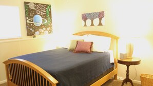 A bedroom with a wooden bed, a blue bedspread, a small bedside table with a lamp, and wall art. - Heritage Suites 43 (Manhattan)
