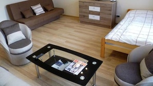 Una habitación pequeña y amoblada con un sofá, una silla, una cama, un televisor y una mesita con una revista.