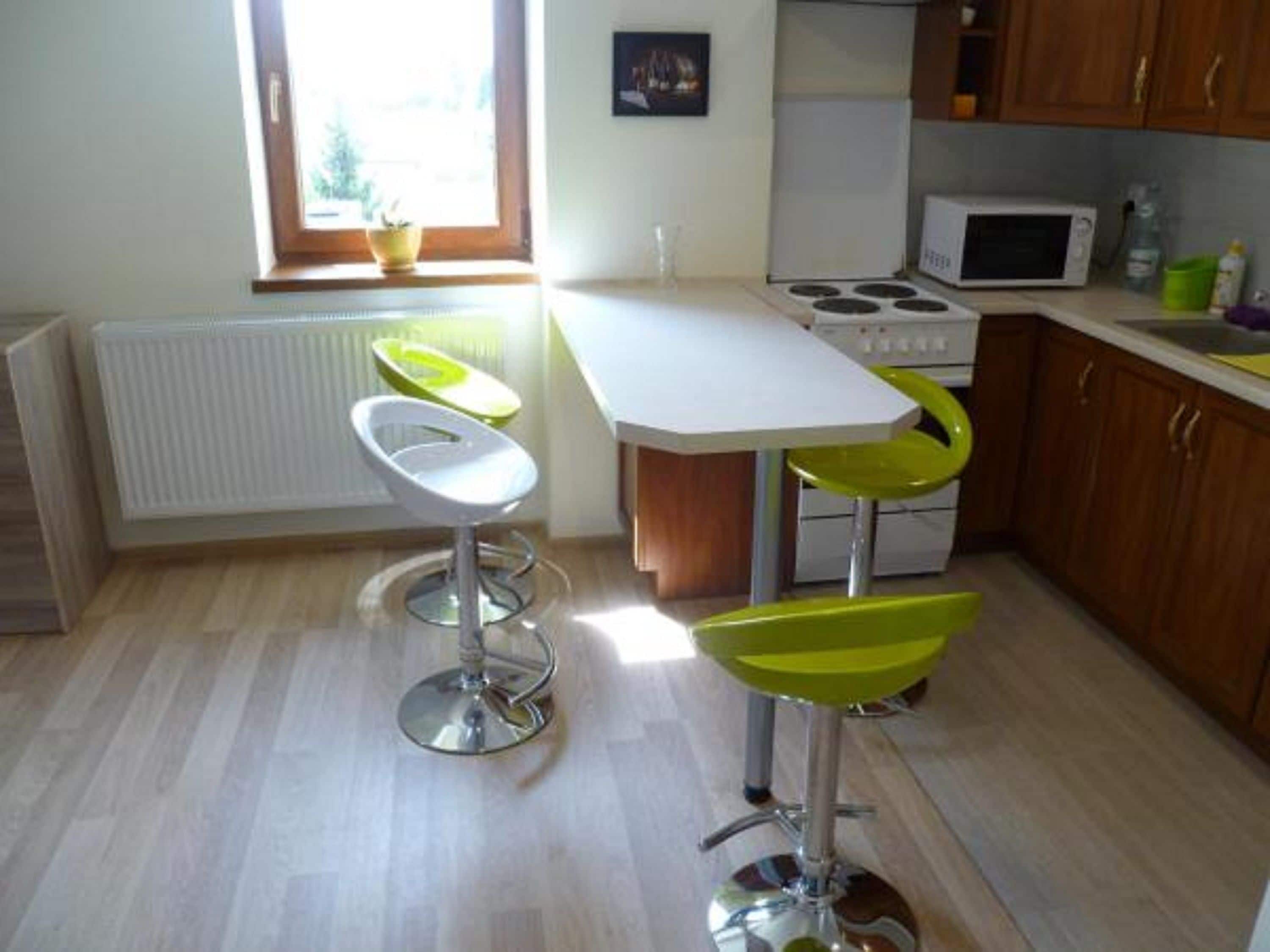 Une cuisine avec un plan de travail blanc, une cuisinière et deux tabourets de bar avec des assises vertes.