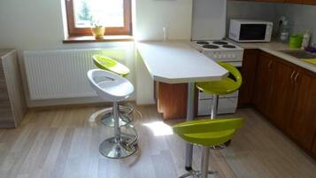 Une cuisine avec un plan de travail blanc, une cuisinière et deux tabourets de bar avec des assises vertes.