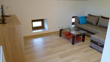 Ein modernes Wohnzimmer mit einem Glastisch, einer Couch mit Kissen, einem kleinen Fenster und einer Holzkommode.