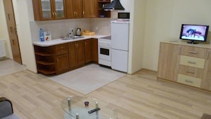 Una cocina compacta con armarios de madera, un refrigerador blanco y un microondas. Hay una mesa de vidrio con un control remoto y un pequeño adorno.