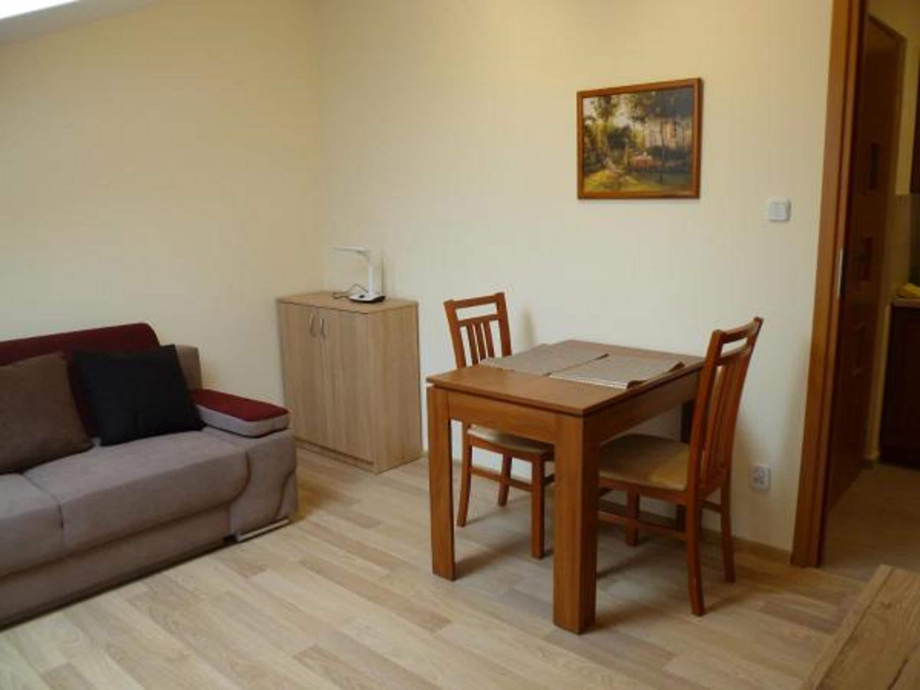 A small, neatly arranged living space with a wooden dining table, two chairs, a sofa, and a cabinet.