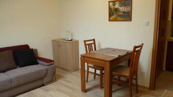 A small, neatly arranged living space with a wooden dining table, two chairs, a sofa, and a cabinet.
