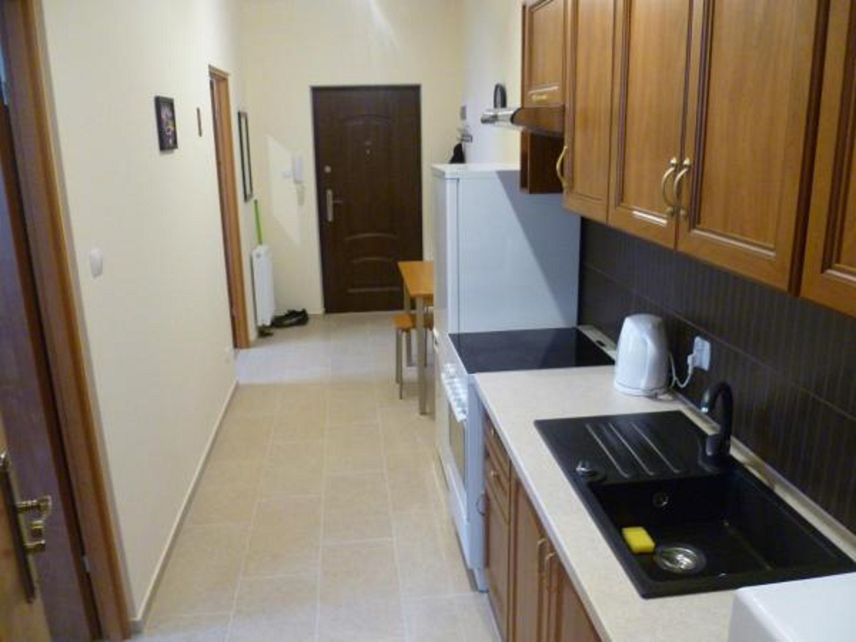 Una cocina estrecha con armarios de madera, un refrigerador blanco y una encimera negra con un fregadero.