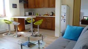 Una cocina moderna con armarios de madera, un refrigerador blanco y un comedor con una mesa de vidrio y sillas verdes.