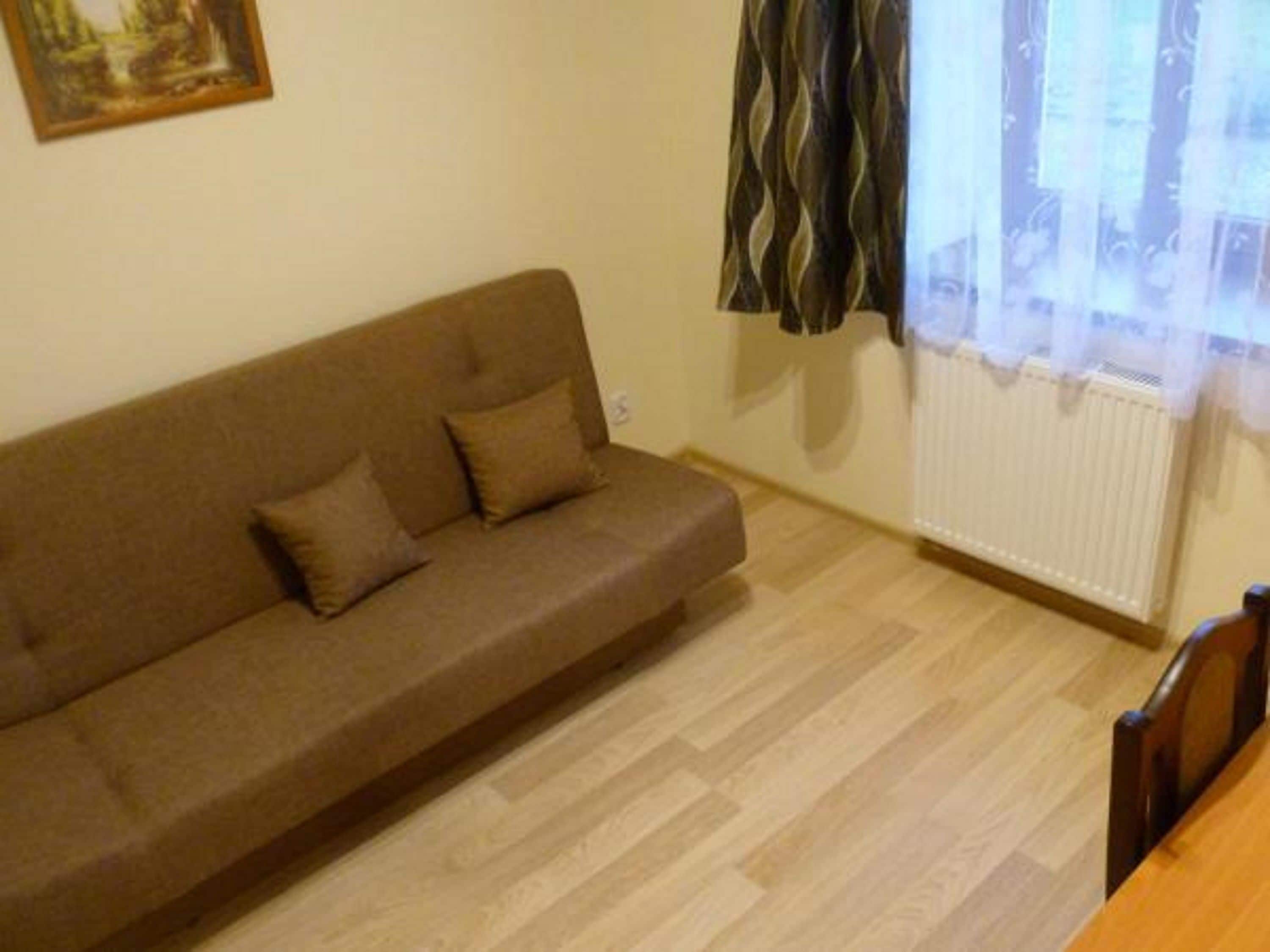 Una sala de estar con un sofá marrón, dos cojines, un radiador y una ventana con cortinas.