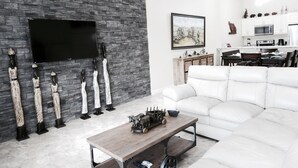 Ein modernes Wohnzimmer mit einer Steinwand, einem Flachbildfernseher, einem weißen Sofa und einem Essbereich mit einer Küche im Hintergrund.