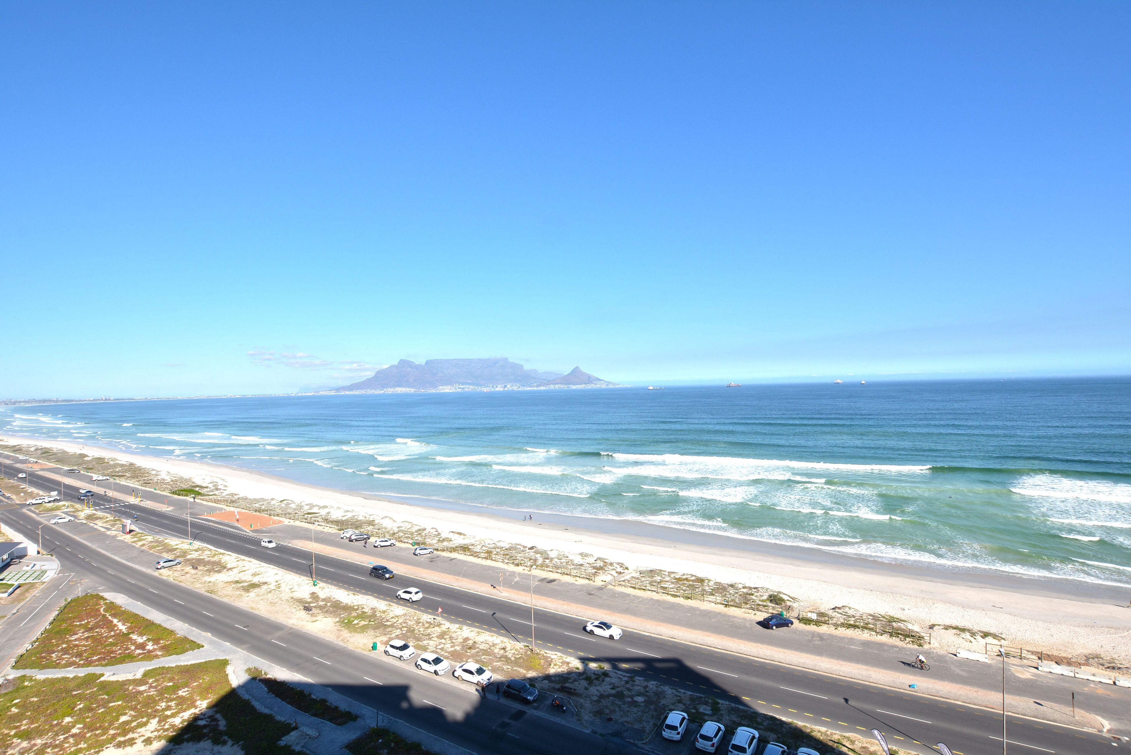 A coastal highway with vehicles, a beach, and ocean waves.