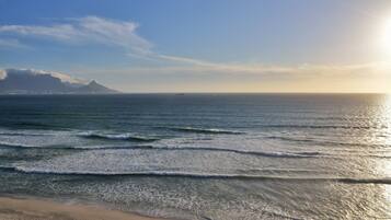 A beach with waves, a distant mountain, and a ship in the distance.