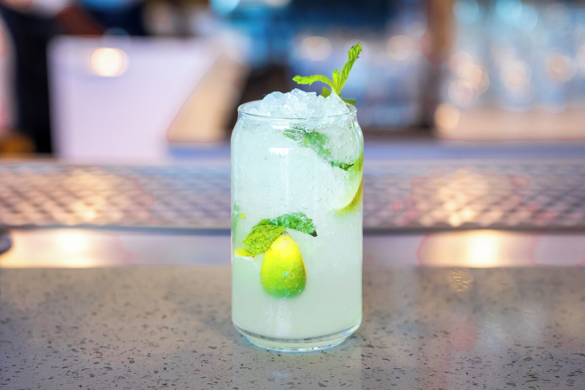 A tall glass with a lime slice and mint garnish on a speckled countertop.