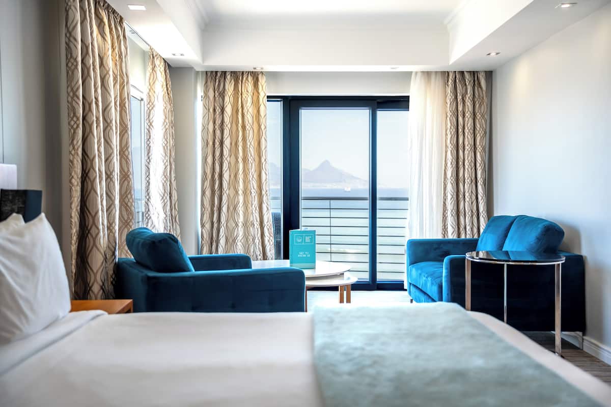 Hotelkamer met een bed, twee blauwe fauteuils, een tafeltje en uitzicht op een berg door grote ramen.