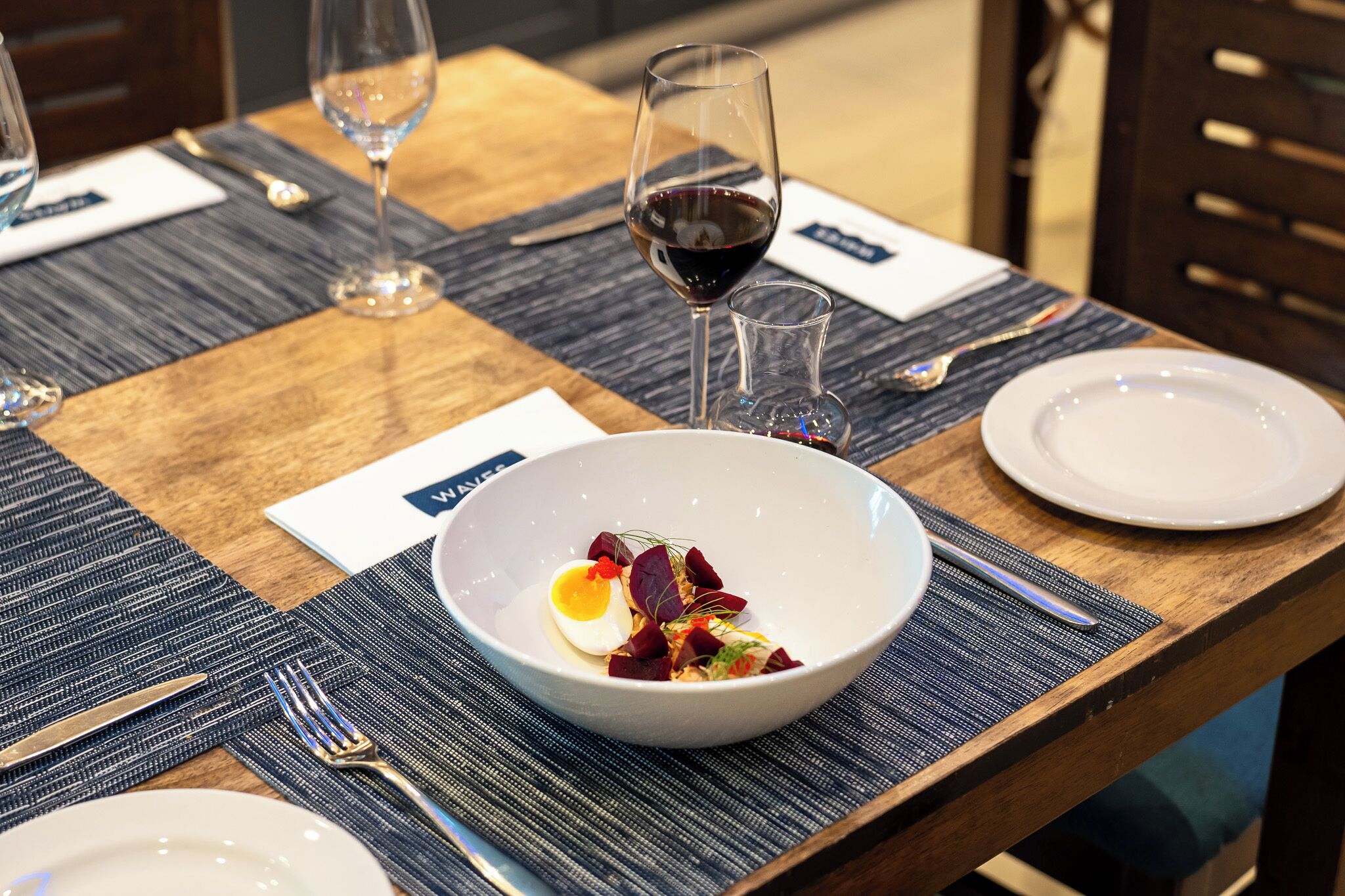 Een eettafel gedekt met een schaal eten, een wijnglas en bestek.
