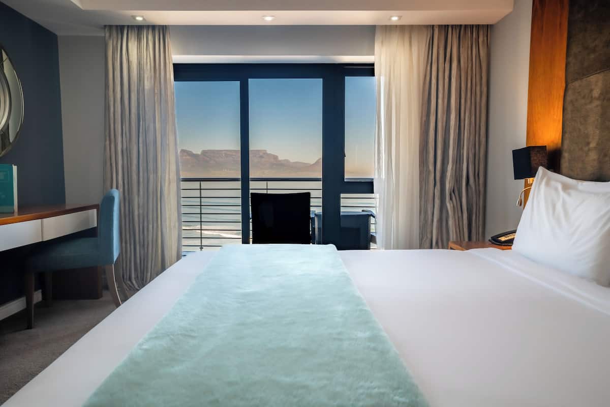 Een hotelkamer met een groot bed, een bureau en een stoel. Vanuit de ramen is er uitzicht op de bergen.