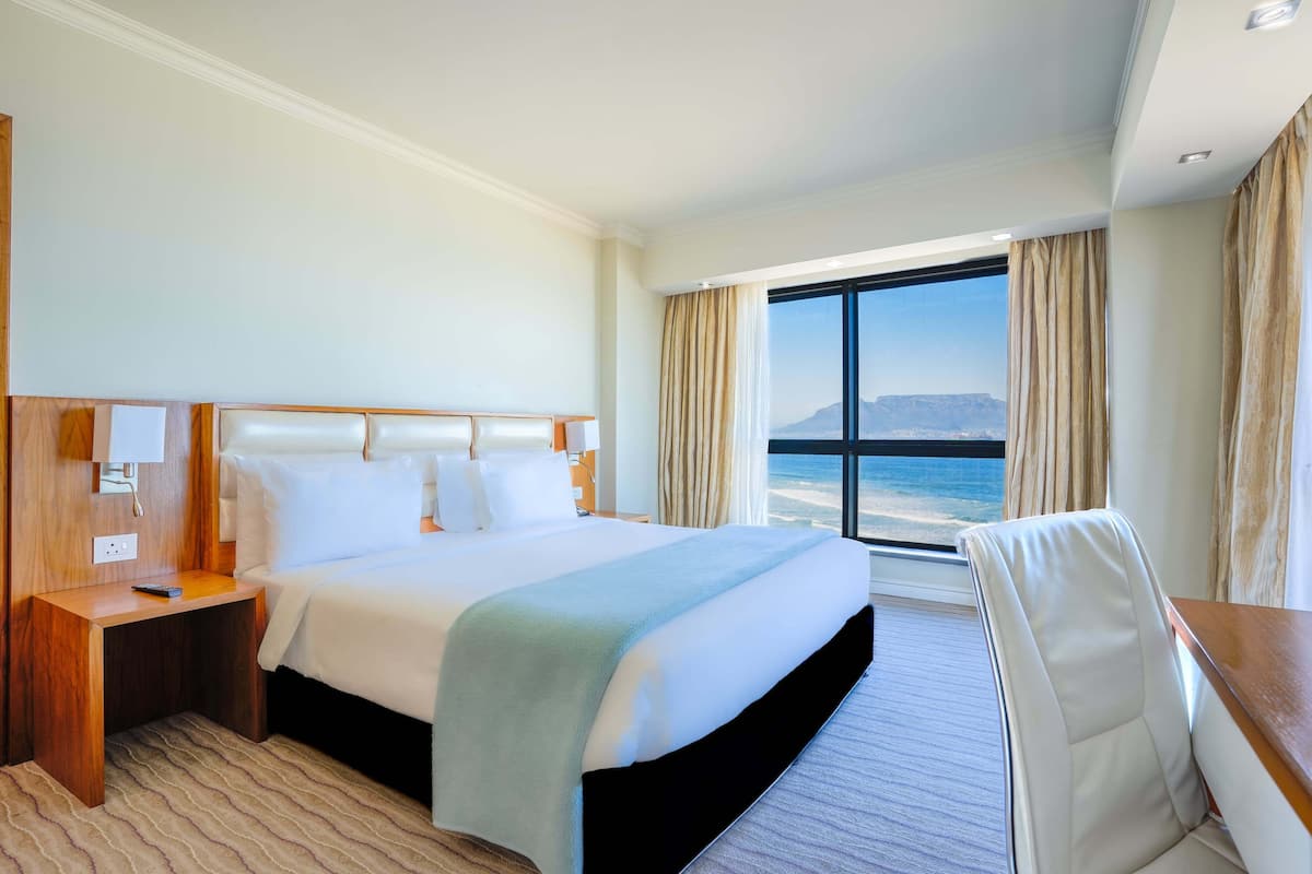 Een hotelkamer met een groot bed, een bureau en uitzicht op de oceaan.