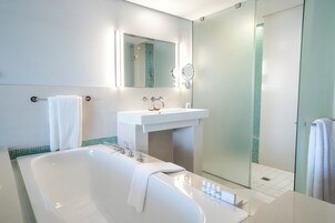 Un baño moderno con una bañera grande, un lavabo, un espejo y una ducha con mampara de vidrio.