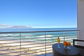 Ein Balkon mit Meerblick, ein Tisch mit Getränken und Obst, und ein Stuhl.