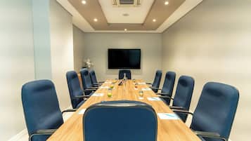 A conference room with a long table, blue chairs, a flat-screen TV, and an air conditioning unit on the ceiling.