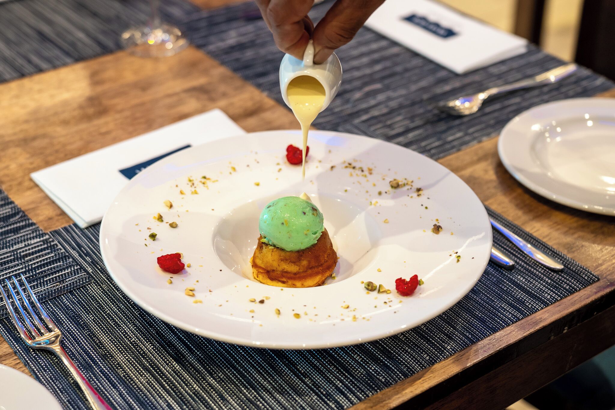 Une assiette à dessert avec une boule de glace verte posée sur un petit gâteau, le tout nappé d’une sauce jaune.