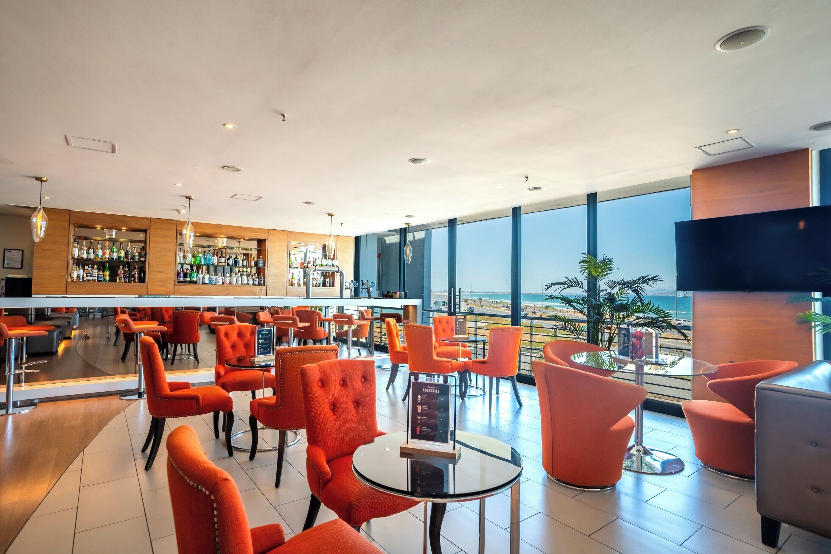 A modern bar area with orange chairs and a bar counter displaying various bottles.
