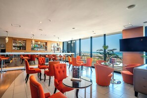 A modern bar area with orange chairs and a bar counter displaying various bottles.