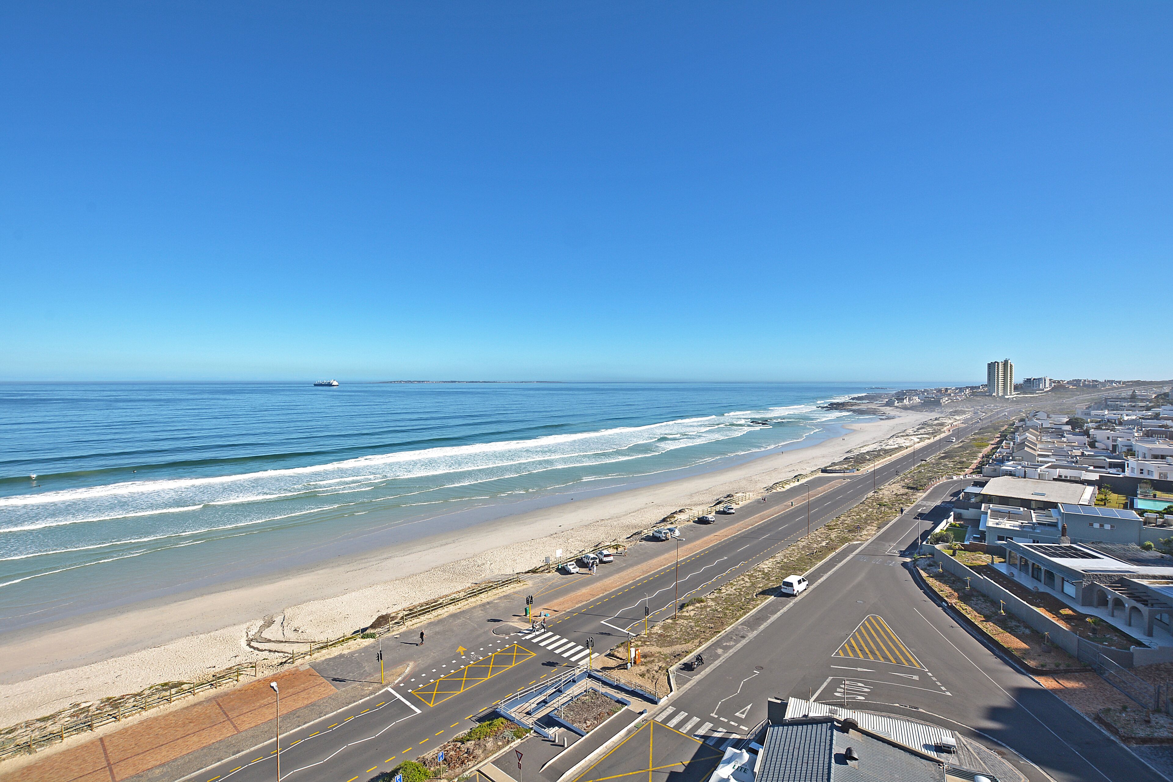 A coastal road with a beach on one side and a row of buildings on the other.