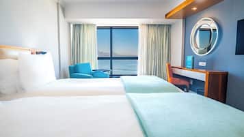 Une chambre d’hôtel avec deux lits, un bureau, une chaise, un miroir et une vue sur la mer.