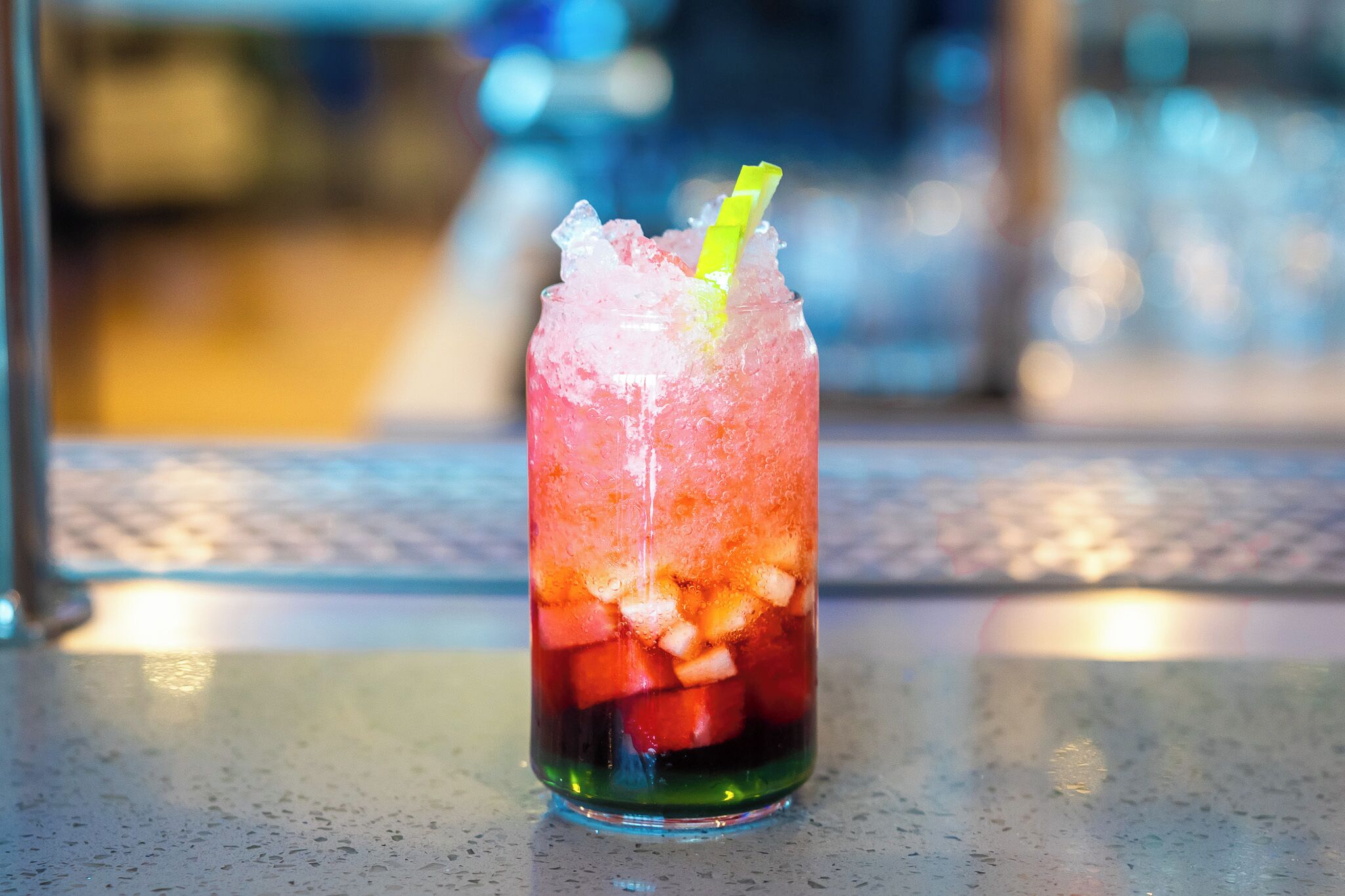 A tall glass with a yellow straw, filled with ice and fruit pieces, placed on a table.