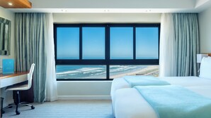Een hotelkamer met een groot raam dat uitzicht biedt op het strand en de oceaan.