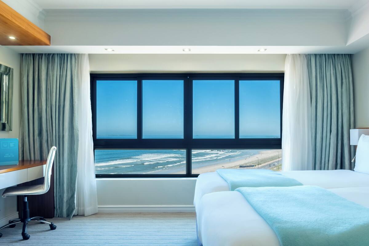 Een hotelkamer met een groot raam dat uitzicht biedt op het strand en de oceaan.
