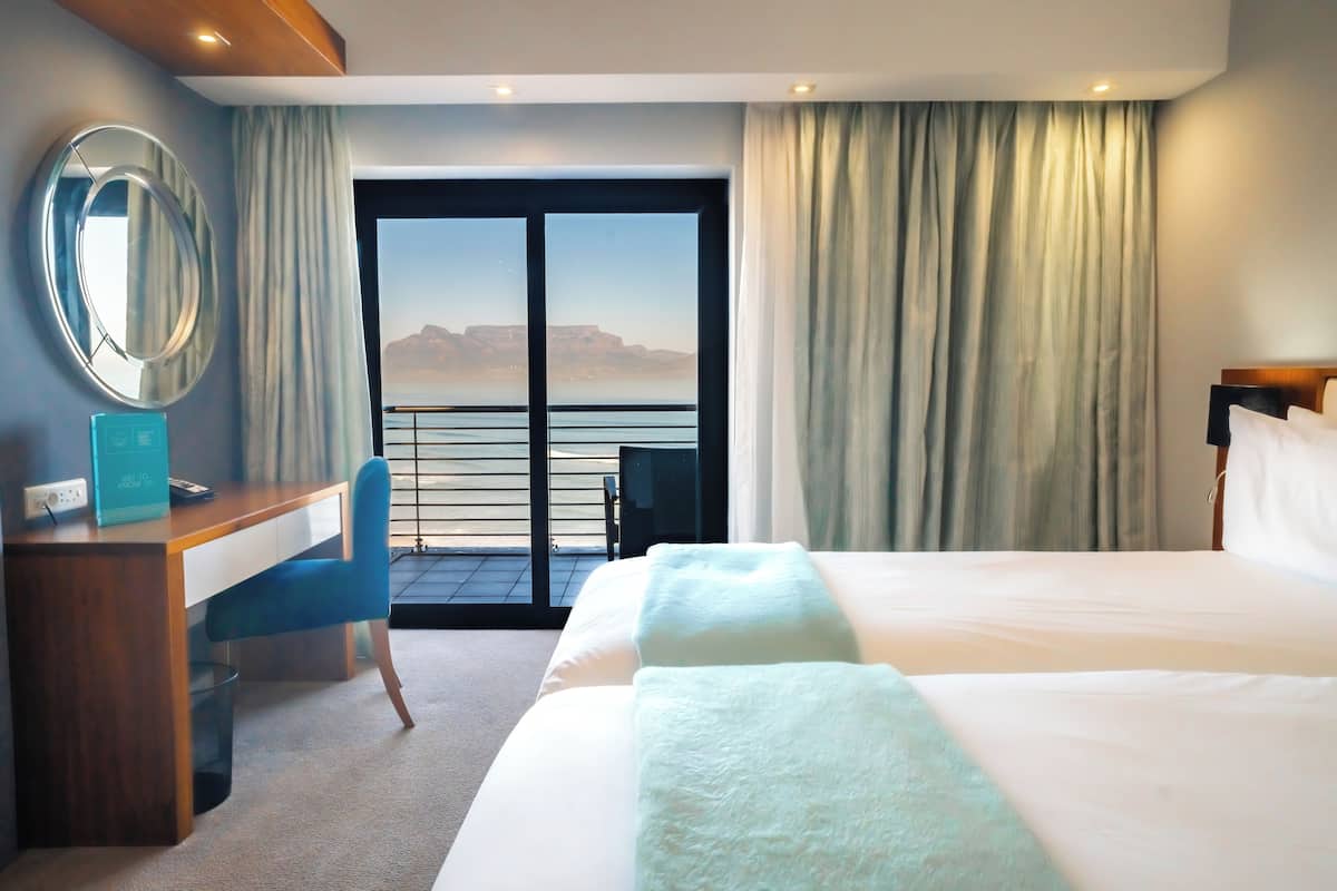 Een hotelkamer met een groot bed, een bureau met stoel, een spiegel en uitzicht op de bergen door het raam.