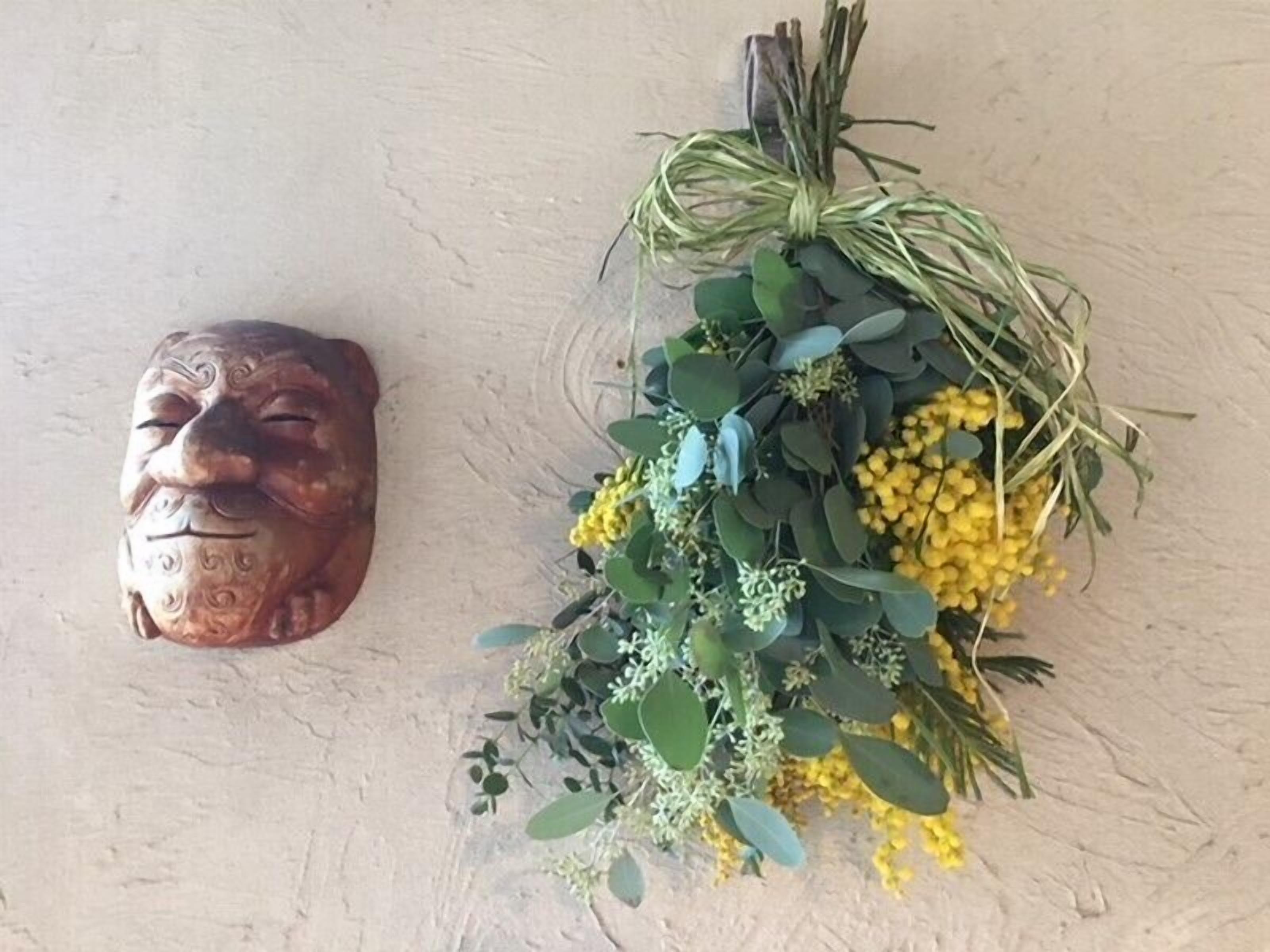 Un masque décoratif fixé au mur et une composition florale avec des feuilles vertes et des fleurs jaunes.