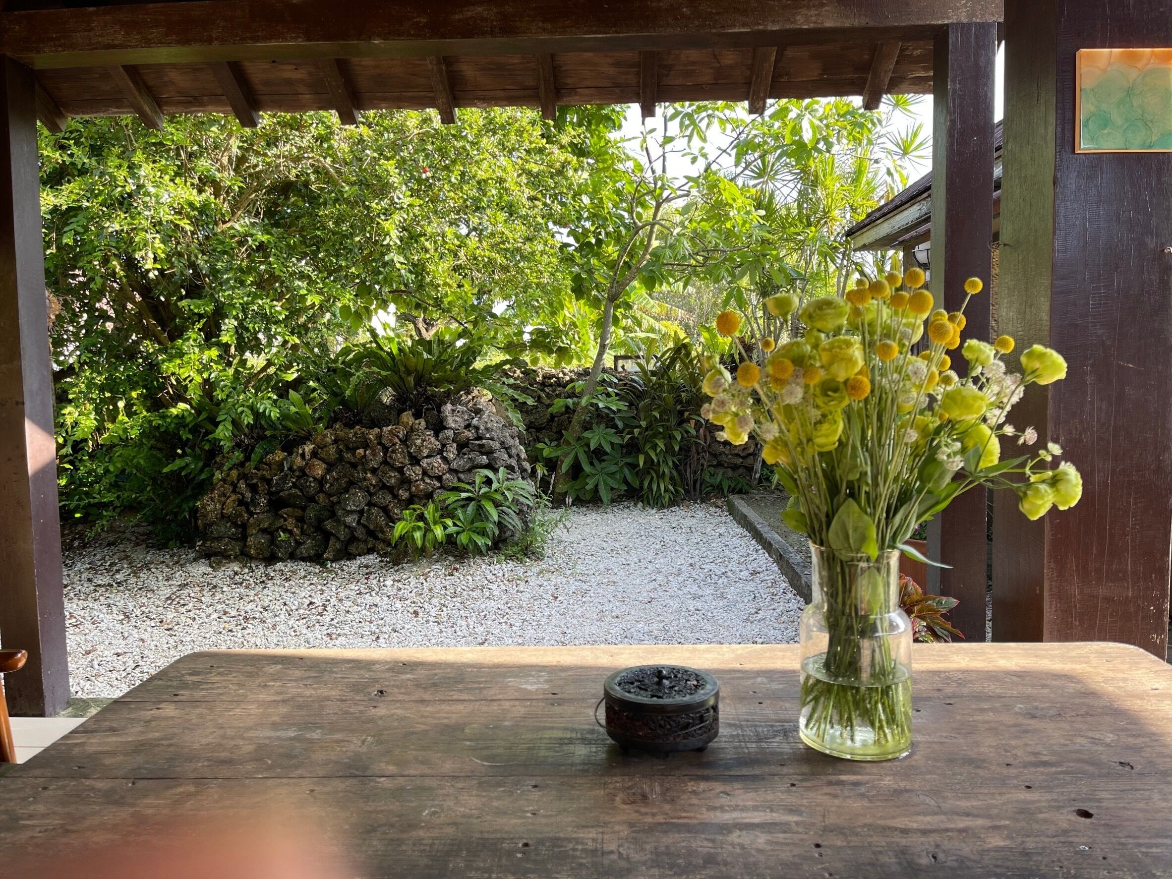 Una mesa de madera con un jarrón de flores amarillas y una pequeña maceta negra.