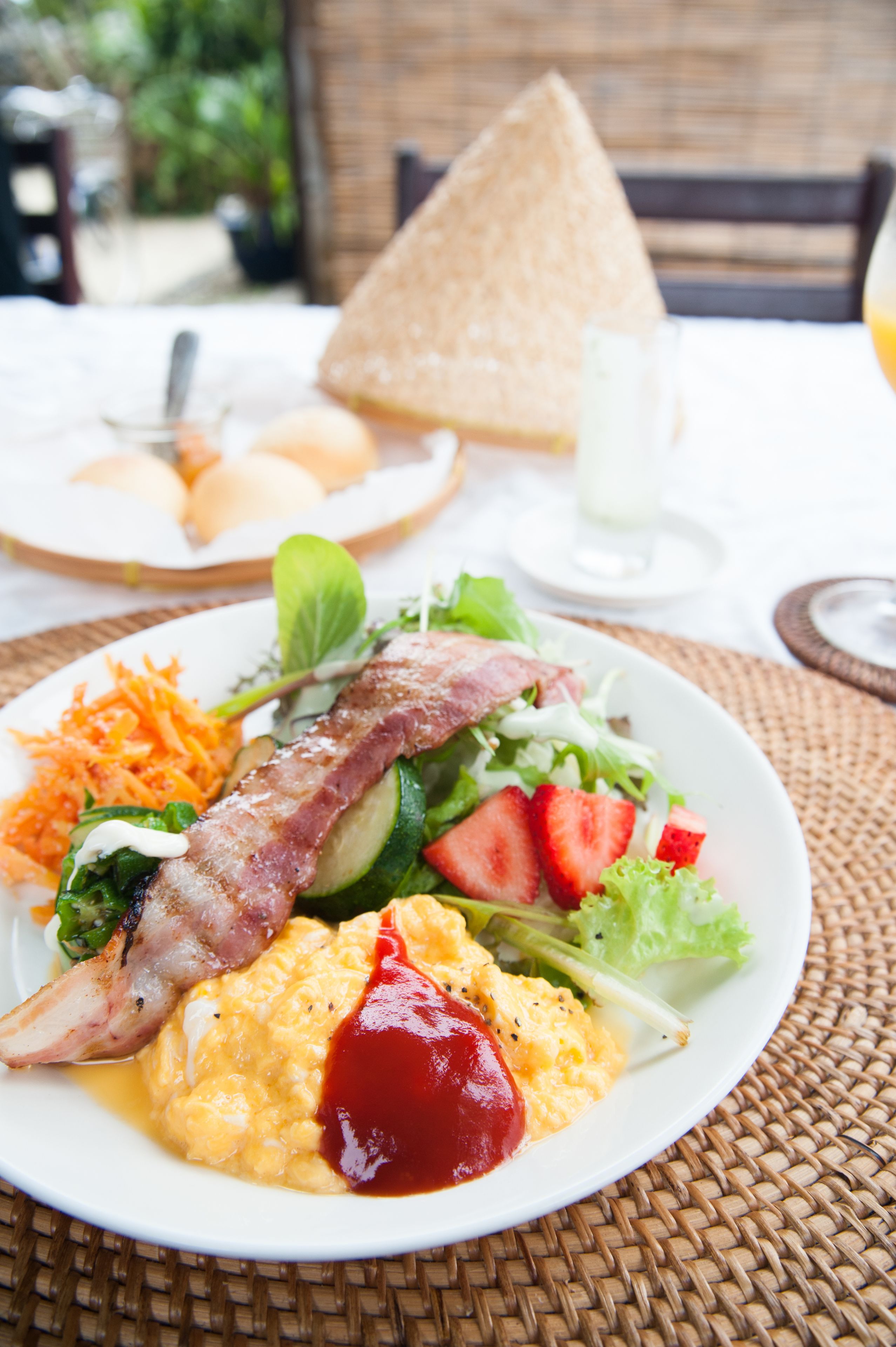 A breakfast plate with scrambled eggs, bacon, strawberries, and a salad.