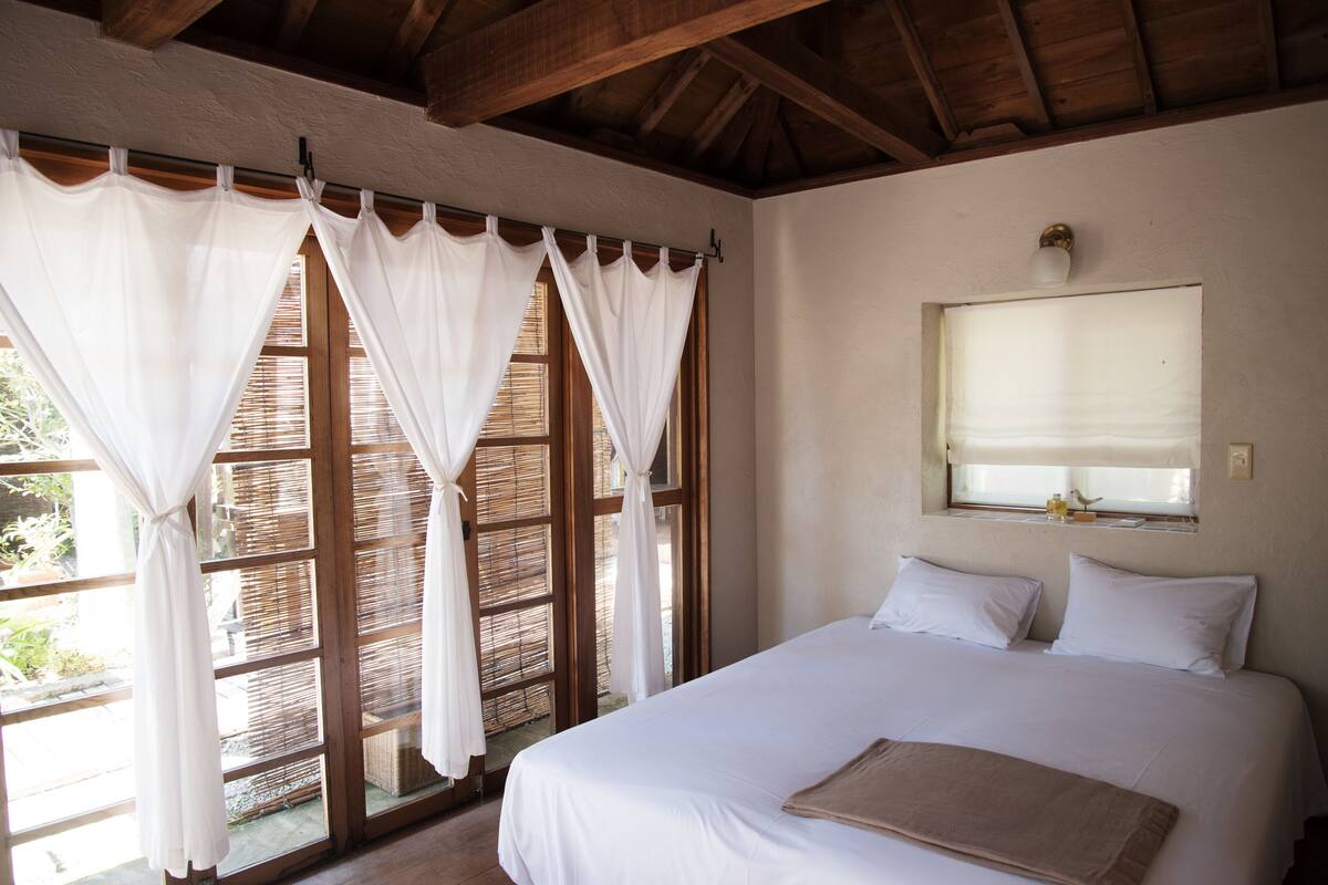 A bedroom with a large bed, white curtains, and a window with a view of the outdoors.